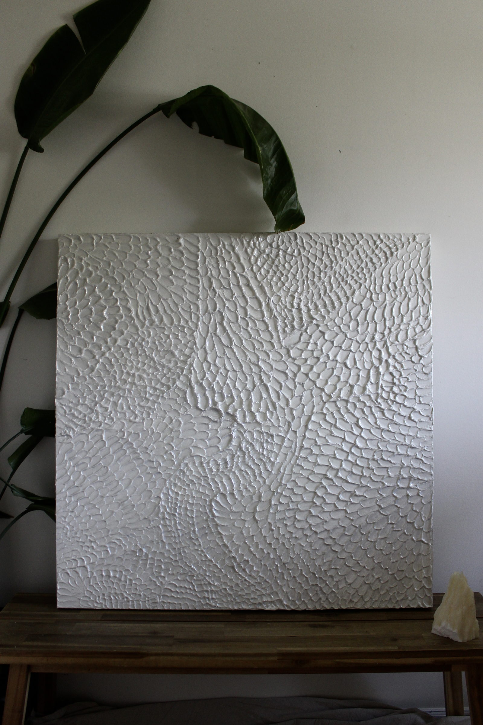 Echo by Jessica Malie, a white sculptural texture canvas resting on a wooden bench