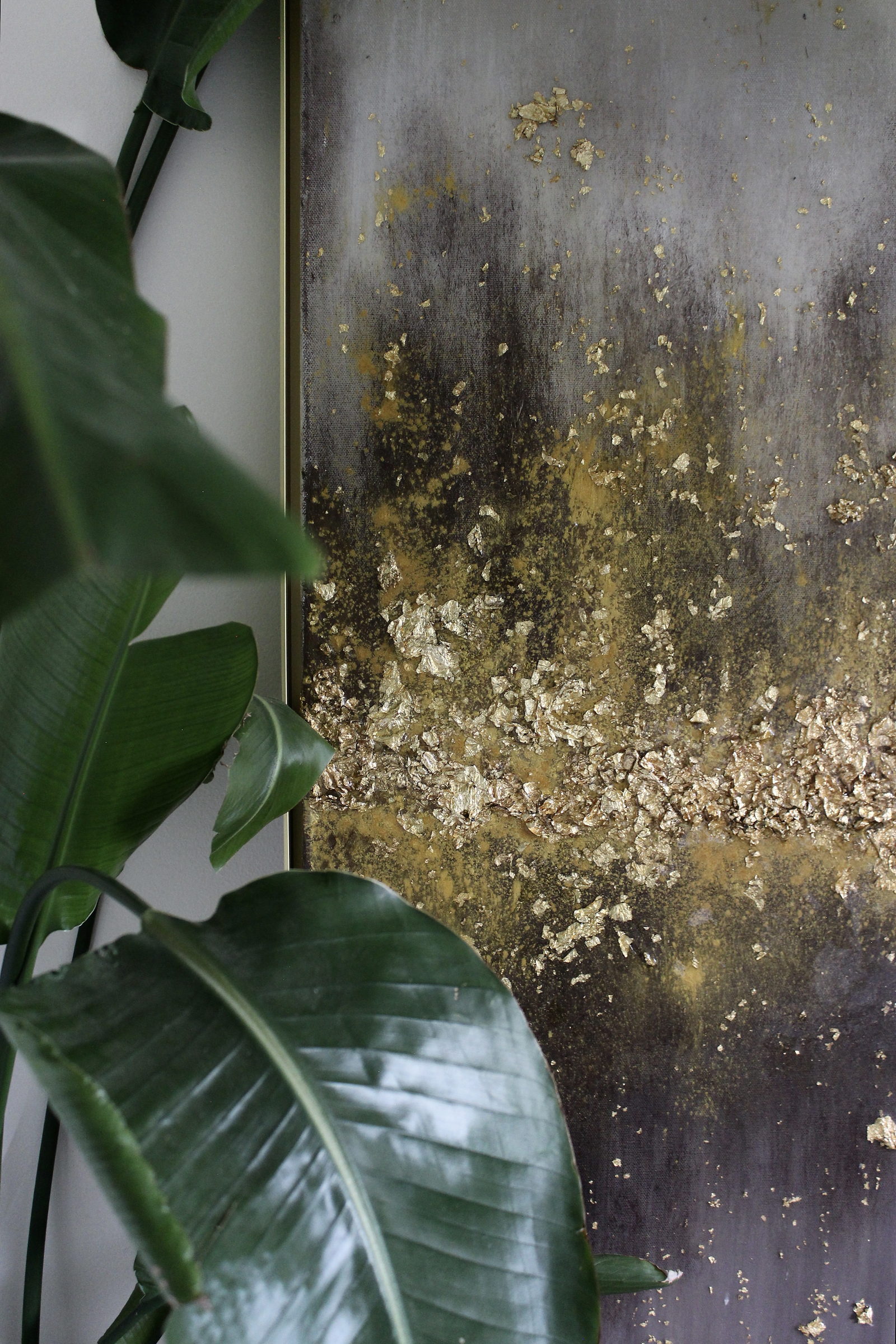 Gilded Earth, gold leaf and resin on canvas, seen past foliage in a residential interior