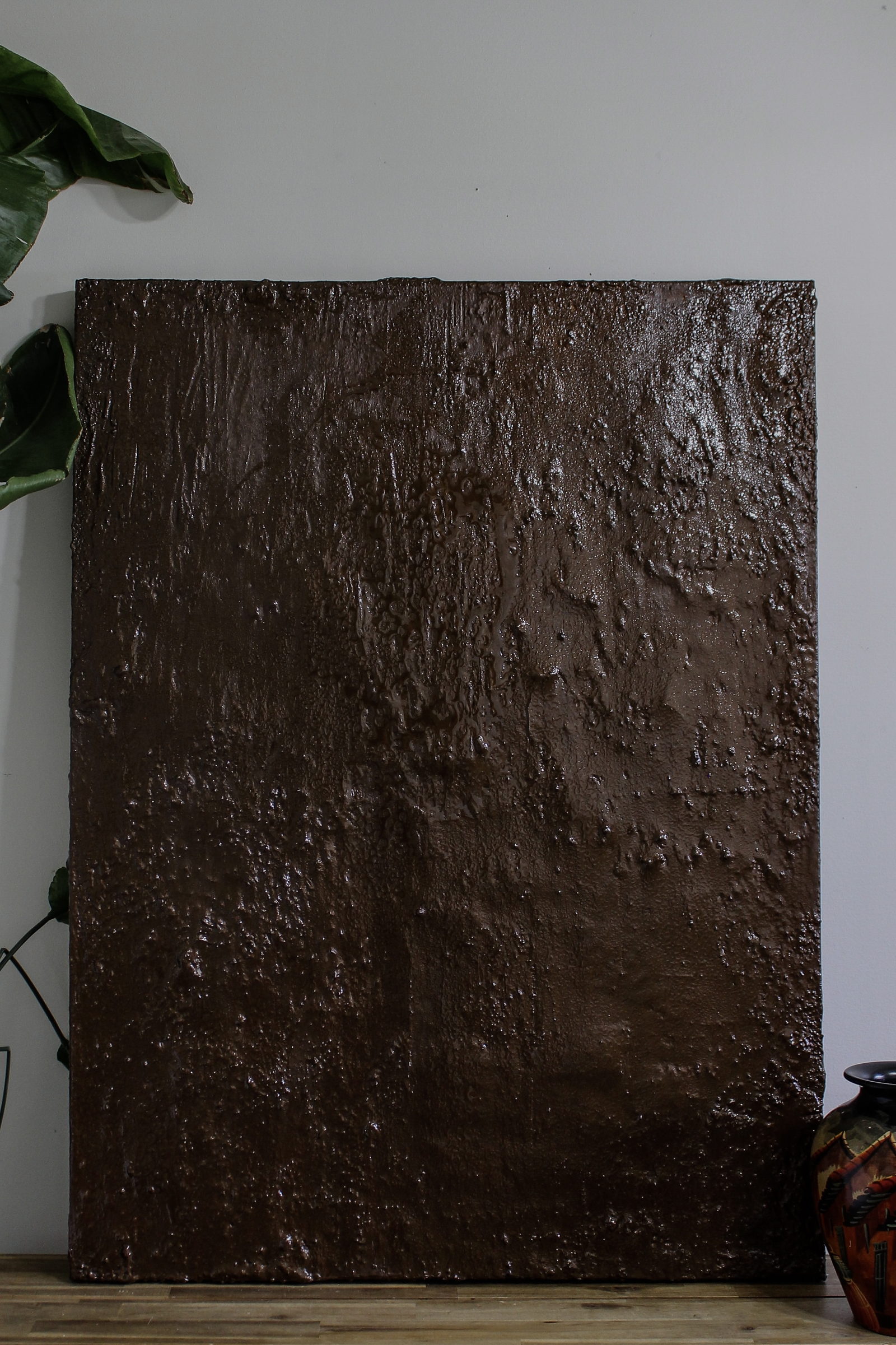Umber by Jessica Malie, a deep brown sculptural texture canvas resting against a wall